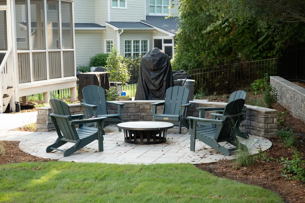 Fire pit patio with Adirondack chairs and a curved stone seat wall beside the screened porch