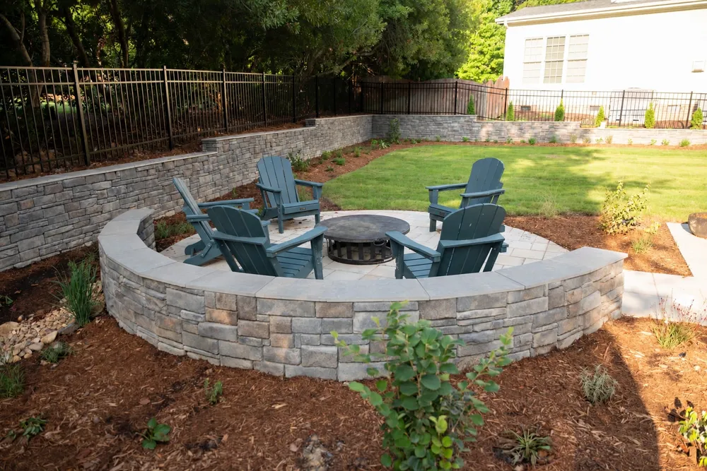 Curved stone seat wall around the fire pit patio, with tiered retaining walls and lawn beyond