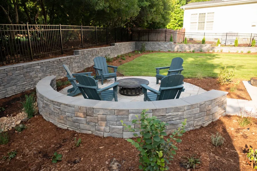 Curved stone seat wall around the fire pit patio, with tiered retaining walls and lawn beyond