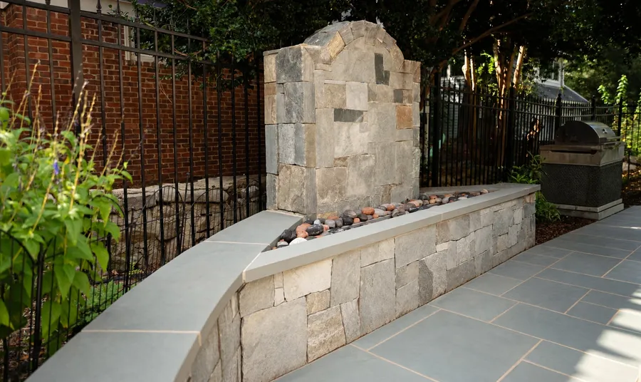 Natural stone fountain wall with a river-rock basin and capped seat wall beside the bluestone patio