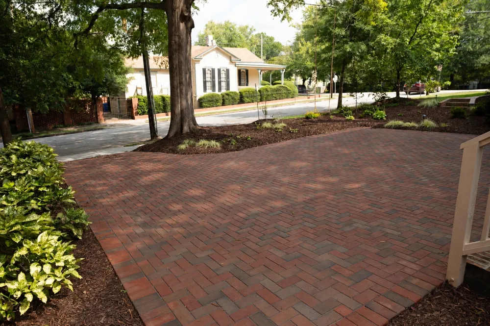 Herringbone brick paver driveway framed by new planting beds under mature trees