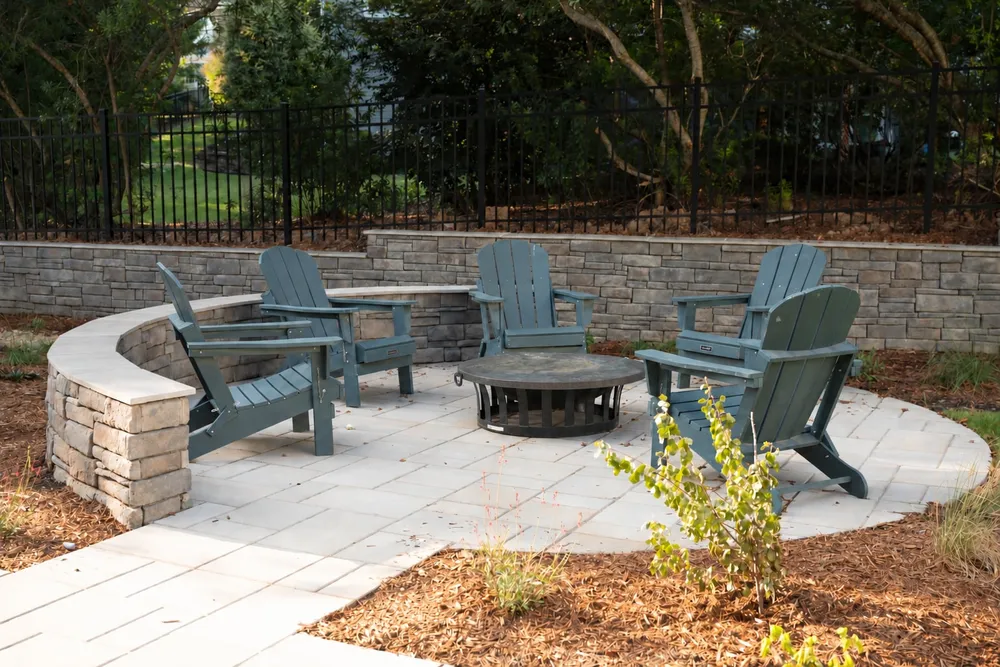 Fire pit patio backed by a stone retaining wall and black metal fence