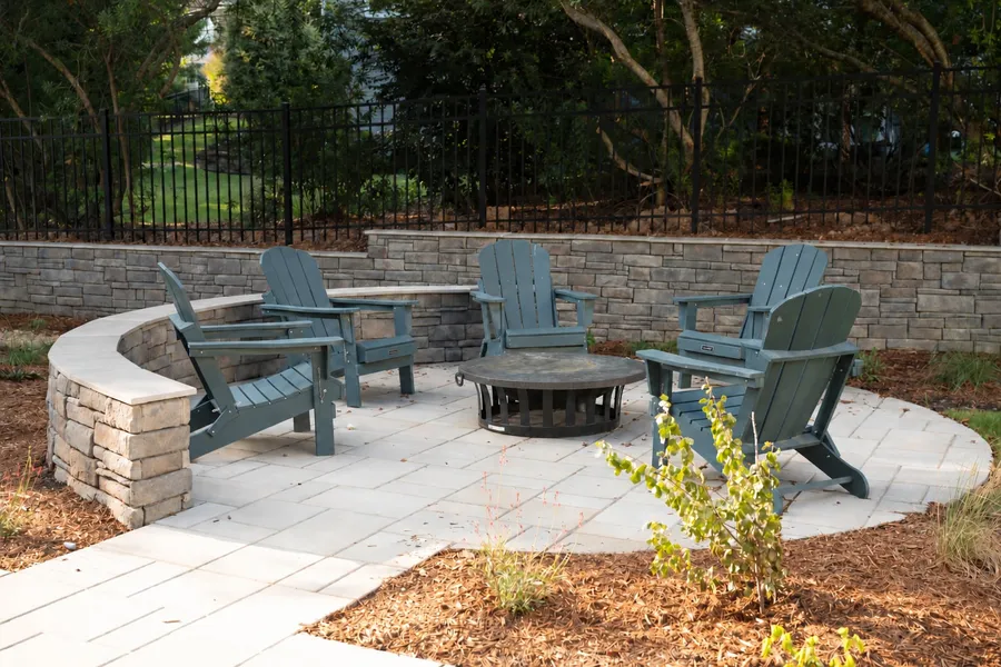 Fire pit patio backed by a stone retaining wall and black metal fence