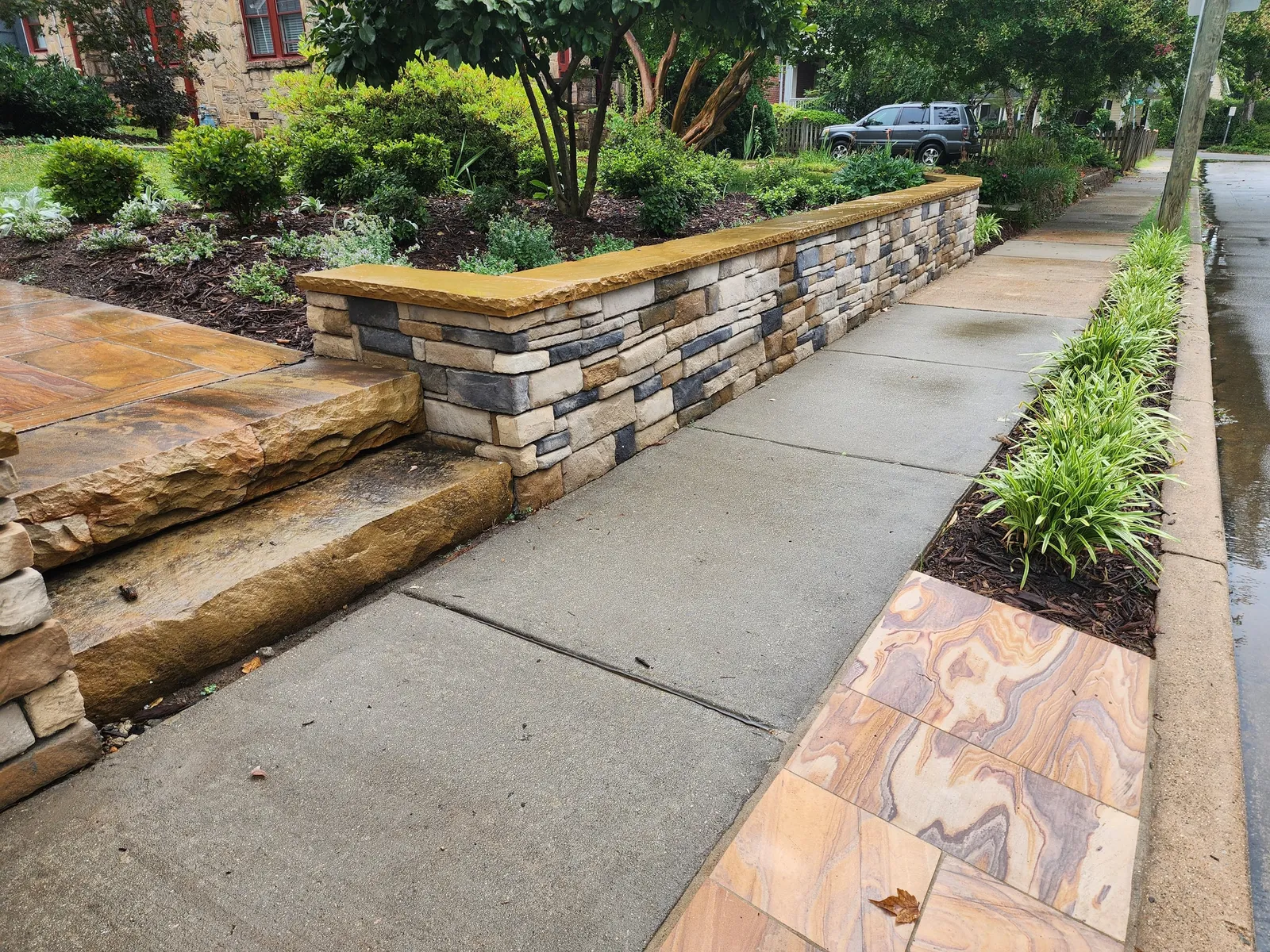 Natural stone slab steps and a rainbow sandstone paver strip alongside the stacked stone wall
