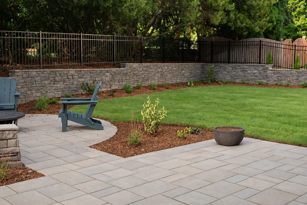 Paver walkway connecting the patio to the fire pit area, with a stone retaining wall along the lawn