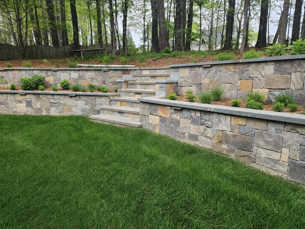 Tiered natural stone retaining walls with built-in stone steps above a green lawn